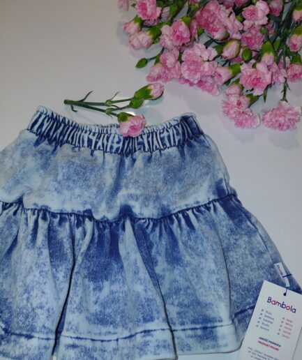 Niebieska spódniczka z falbankami i metką Bambola, obok różowe goździki.